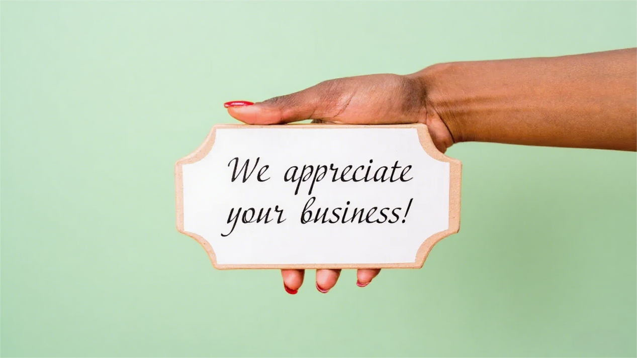 Close-up of a hand holding a sign that reads 'We appreciate your business!' against a light green background